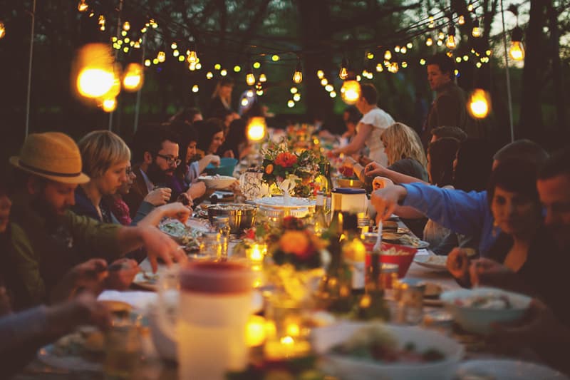 Guests dining at a long outdoor table under warm string lights during a festive evening.